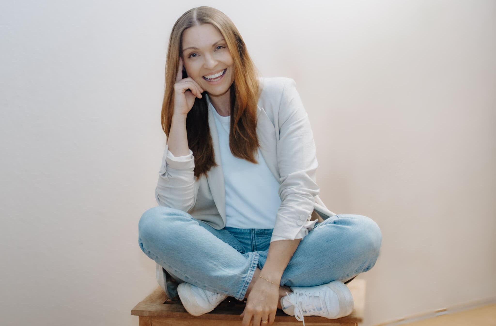 Frau Traurednerin mir langen braunen Haaren sitzt mit gekreuzten Beinen auf iem Stuhl und lächelt in die Kamera.